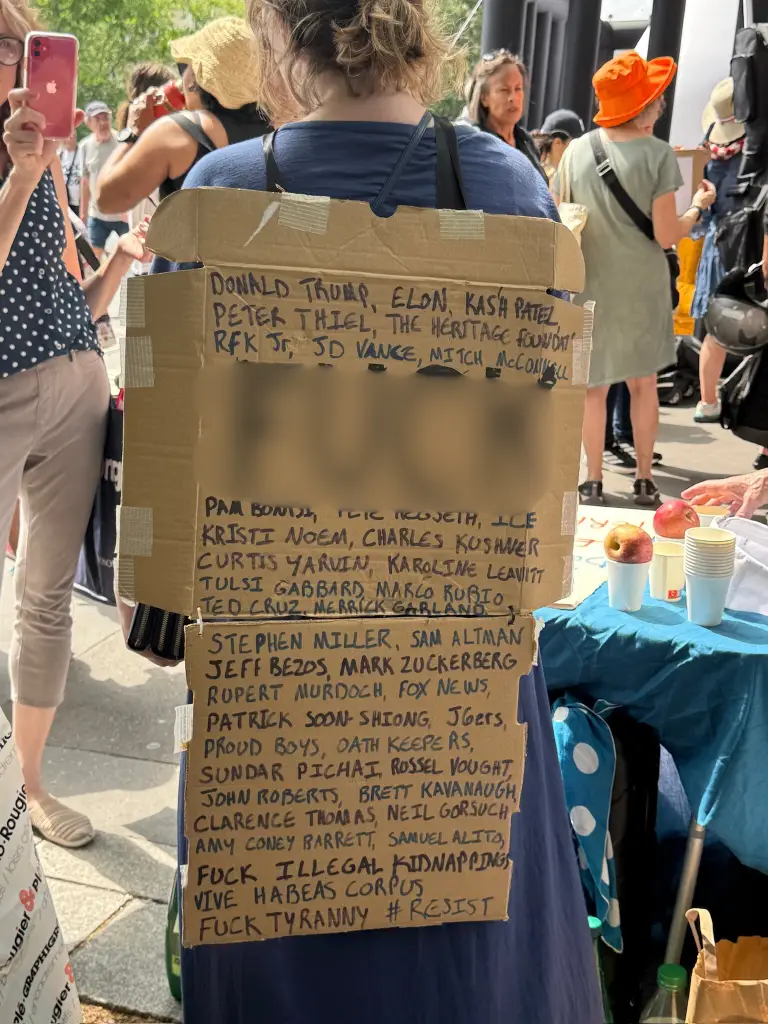 a protester wearing a sign condemning those complicit in the trumpian régime
