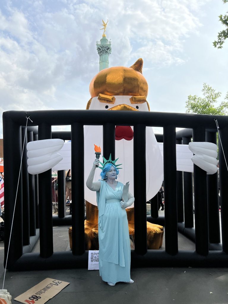 a woman dressed as lady liberty stand in front of the felon chicken art piece by artist taran brar