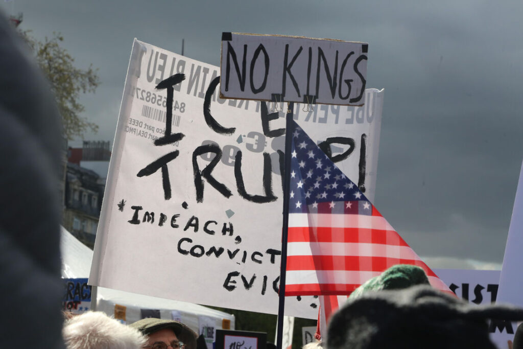 Photo shows anti ICE signs and an American flag. Photo credit: Owen Franken